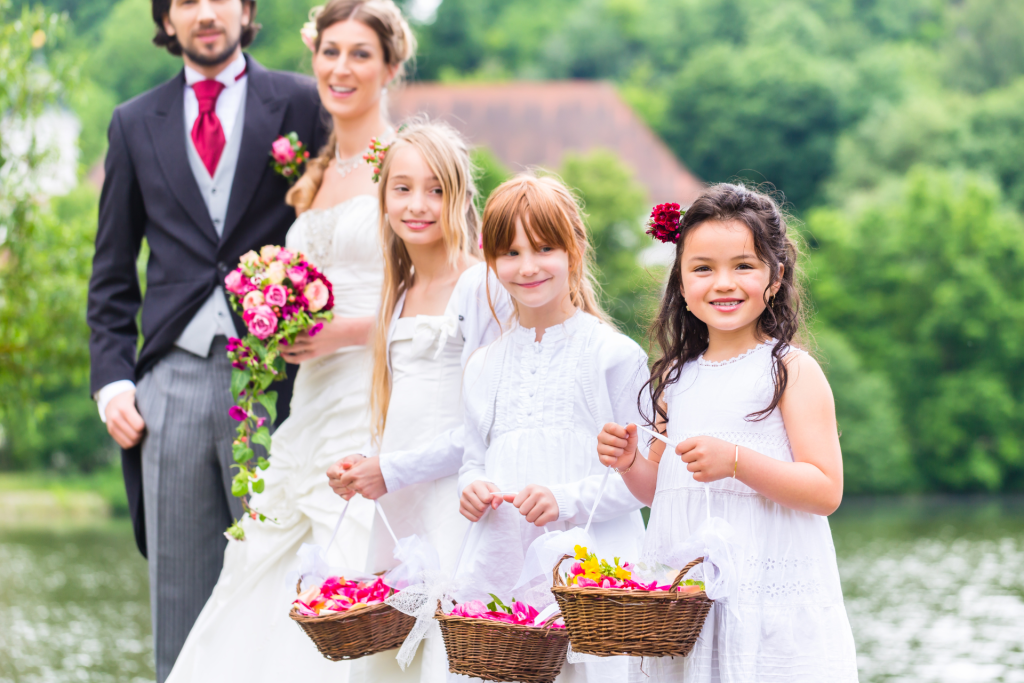 Young flower girls holding baskets filled with petals at a wedding, with the couple visible in the background during the ceremony