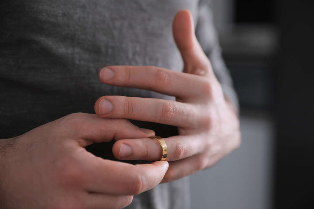 A close-up of a man’s hands as he removes his wedding ring, symbolizing a change in marital status