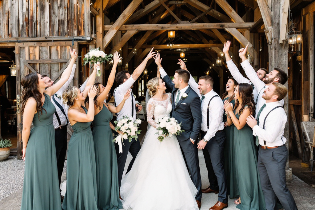 A bride and groom standing at the center of their wedding celebration, surrounded by friends and bridesmaids, all smiling and cheering together