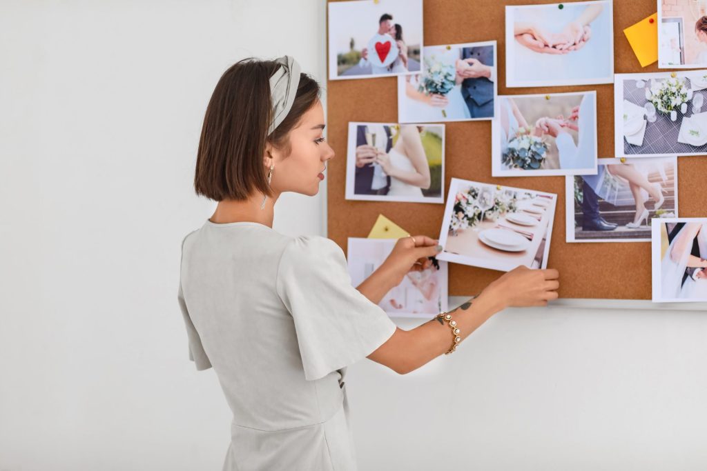 A woman pinning images onto a board while planning her wedding, organizing inspiration for decor, style, and overall theme