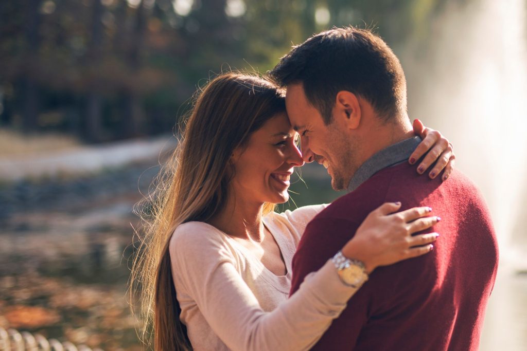 A couple hugging and looking into each other’s eyes on a sunny day, with a softly blurred background creating a romantic atmosphere