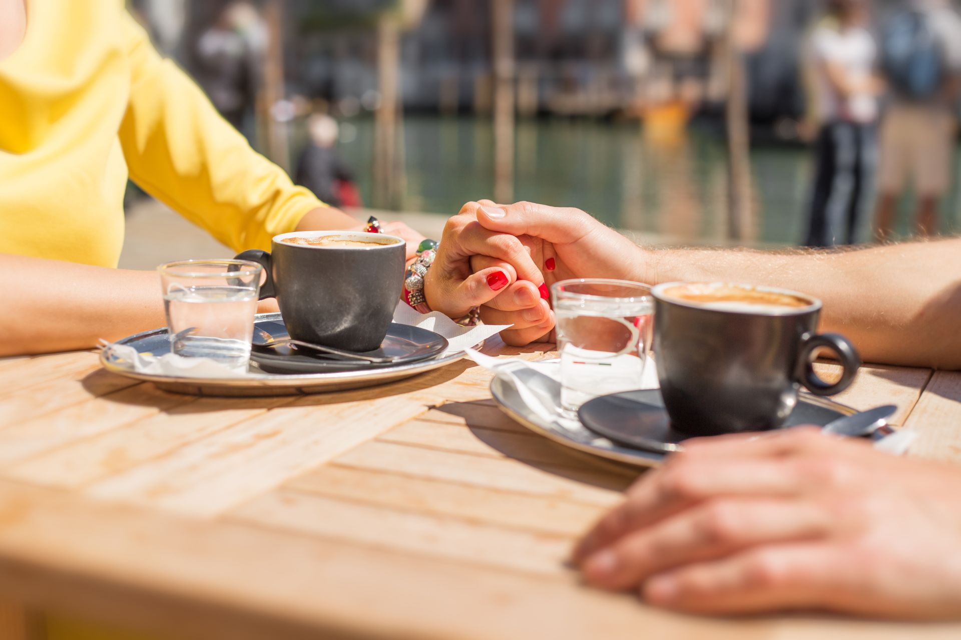 A close-up of two people holding hands across a table with two cups of coffee visible, capturing a warm and intimate moment
