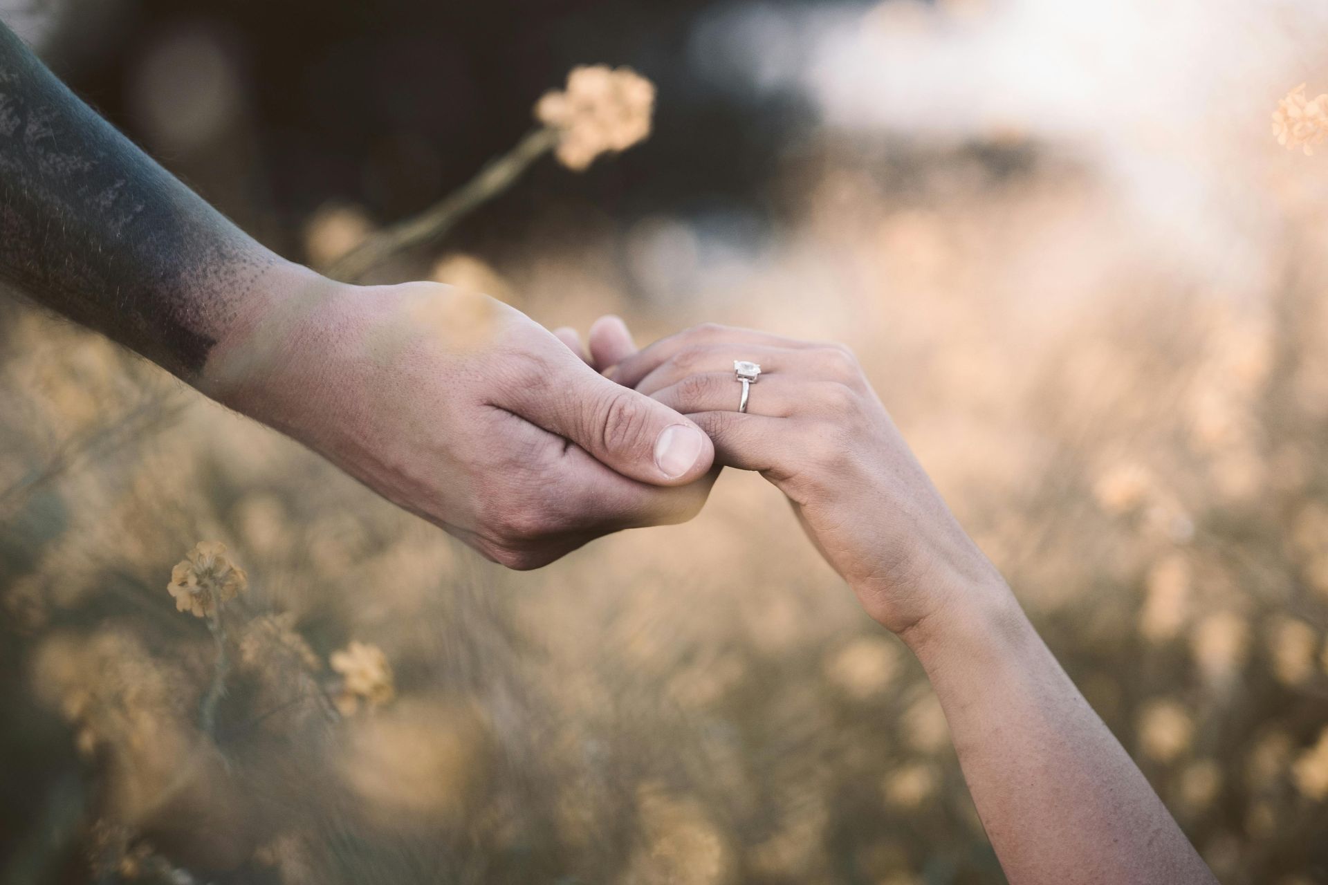 A close-up of two people holding hands, with the woman wearing an engagement ring, showing only their hands in an intimate moment