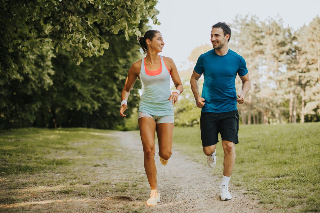 A couple running side by side while jogging through a park, exercising together outdoors