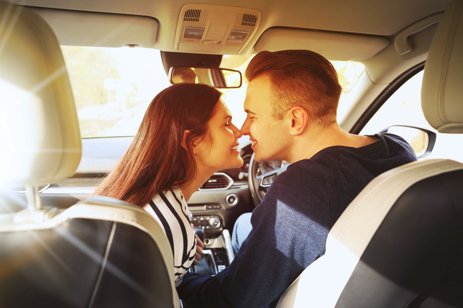 A couple sharing a kiss inside a car with sunlight streaming in, creating a warm and romantic moment