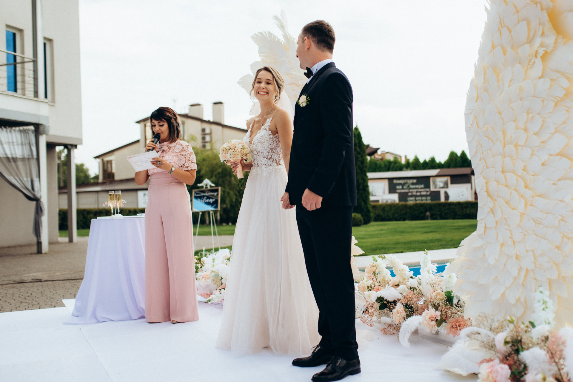 A bride and groom attentively listening as a woman reads a passage during their wedding ceremony, creating a meaningful moment