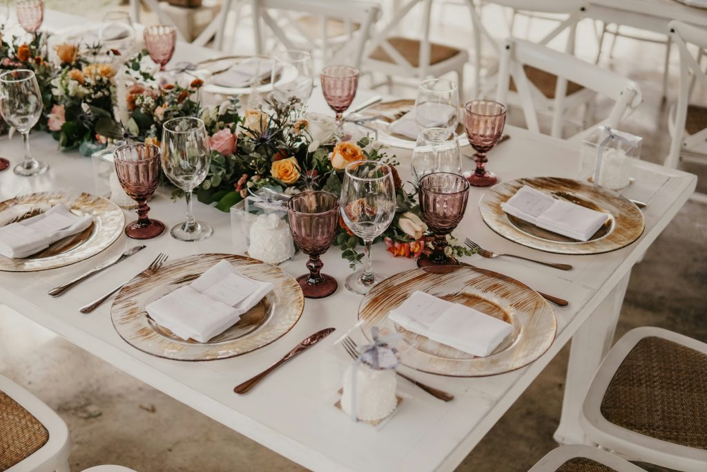 A beautifully arranged wedding table featuring floral centerpieces, glassware, plates, and neatly folded napkins as part of the reception decor