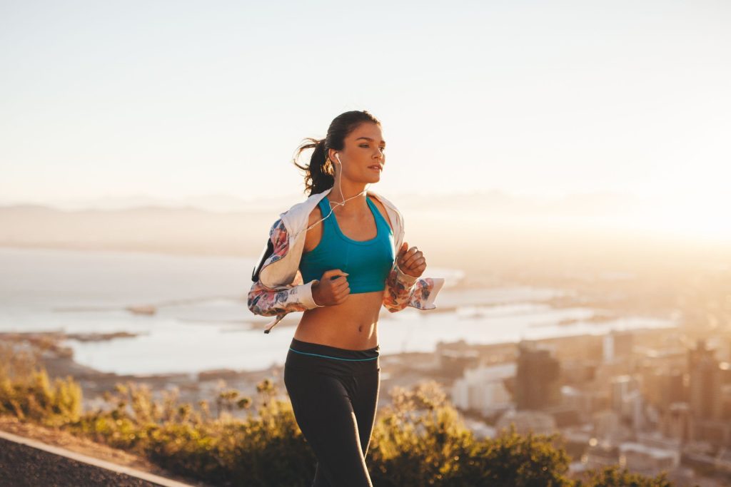 A woman jogging outdoors in the morning while listening to music through headphones, enjoying an active and energetic start to her day
