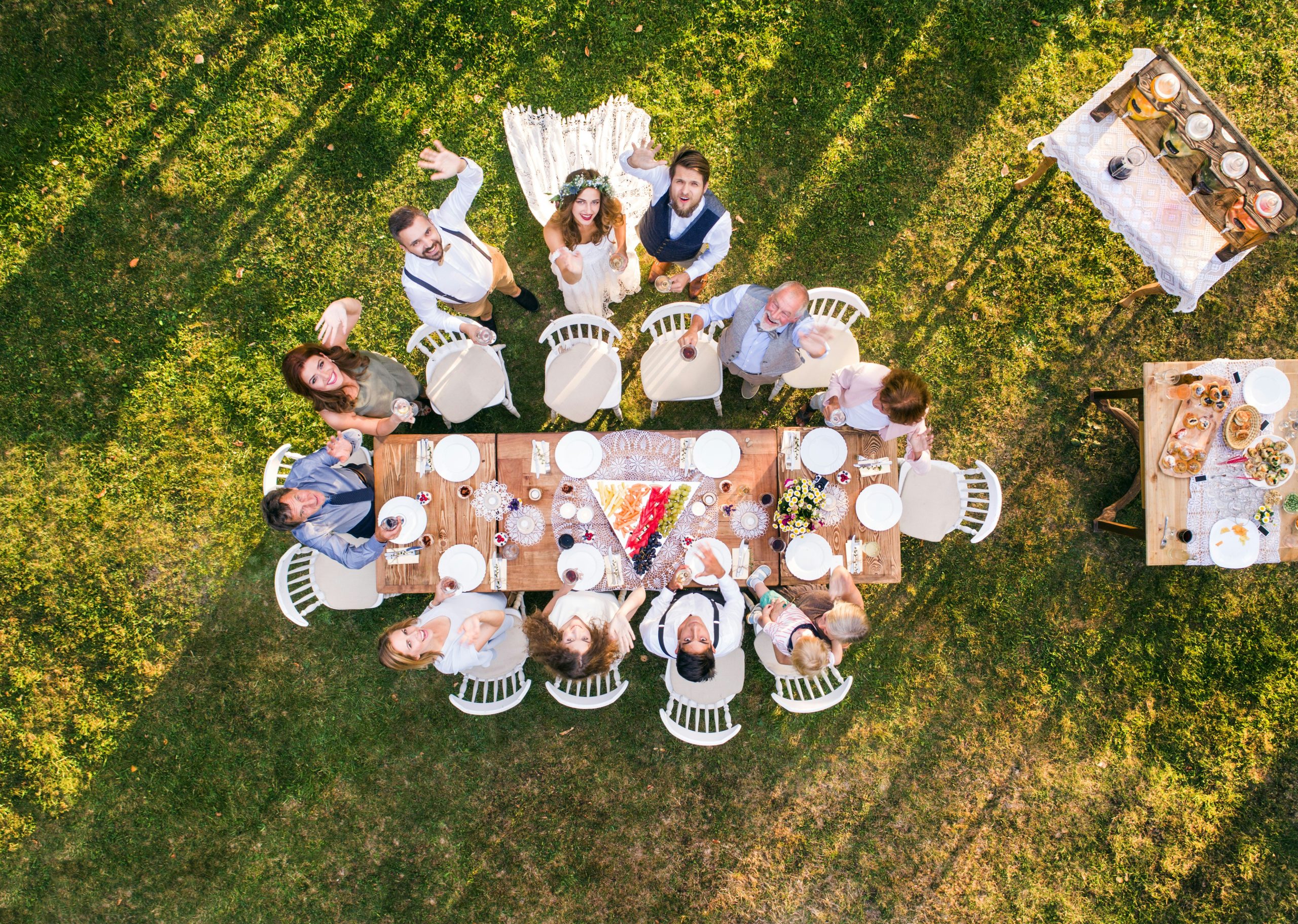 A top-down drone shot of a wedding where the couple and their friends look up and smile at the camera, capturing a joyful group moment