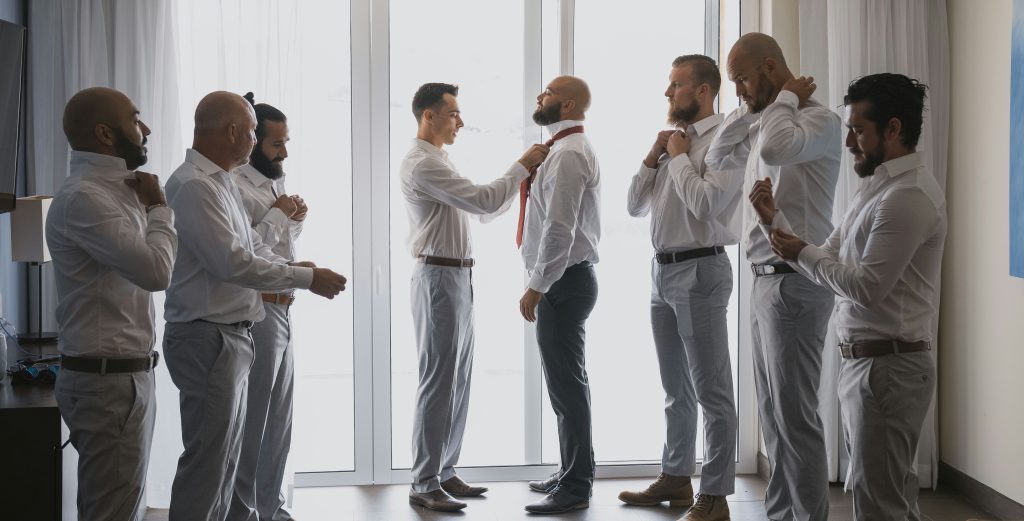 A best man helping the groom adjust his bow tie, capturing a preparation moment before the wedding ceremony