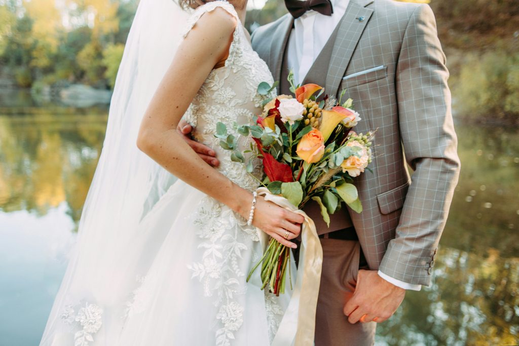 A close-up of a bride and groom’s hands on their wedding day, with the bride holding a bouquet of flowers, highlighting a romantic detail