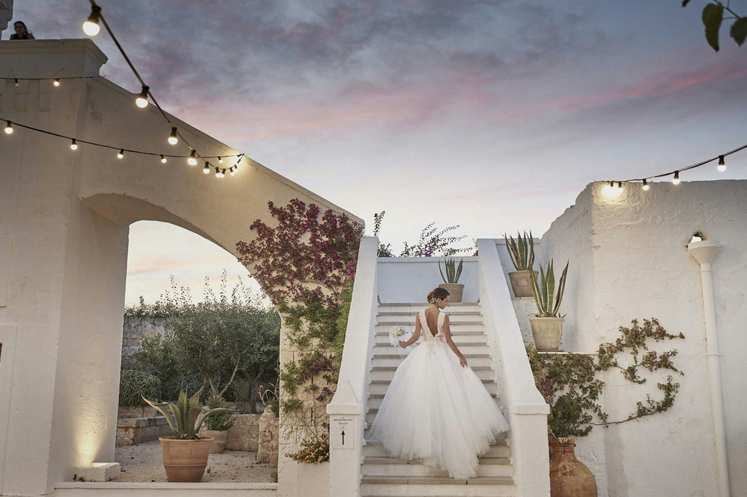 A bride walking up the stairs of a beautiful white historic building decorated with lights, creating an elegant wedding setting