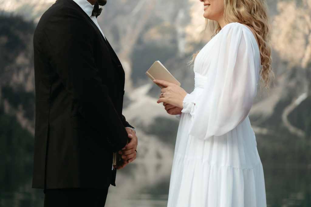 A close-up of the bride’s hands holding a small book as she reads her vows during an outdoor wedding ceremony surrounded by nature