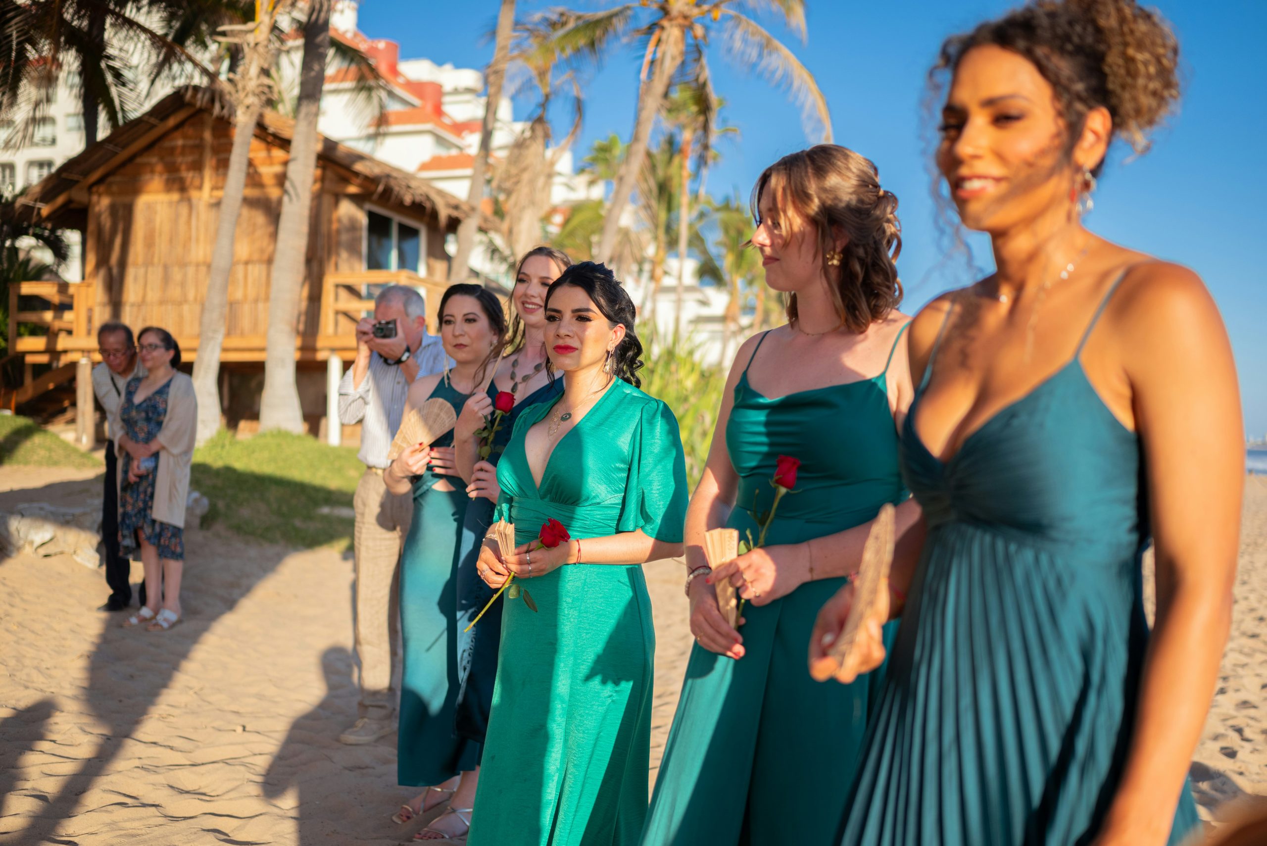 Bridesmaids dressed in blue and green standing in line on the beach, waiting as the wedding ceremony is about to begin