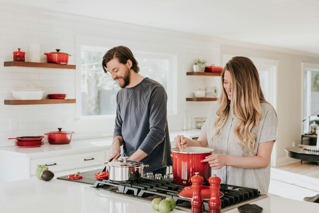 A couple cooking side by side in the kitchen, smiling and talking while enjoying time together