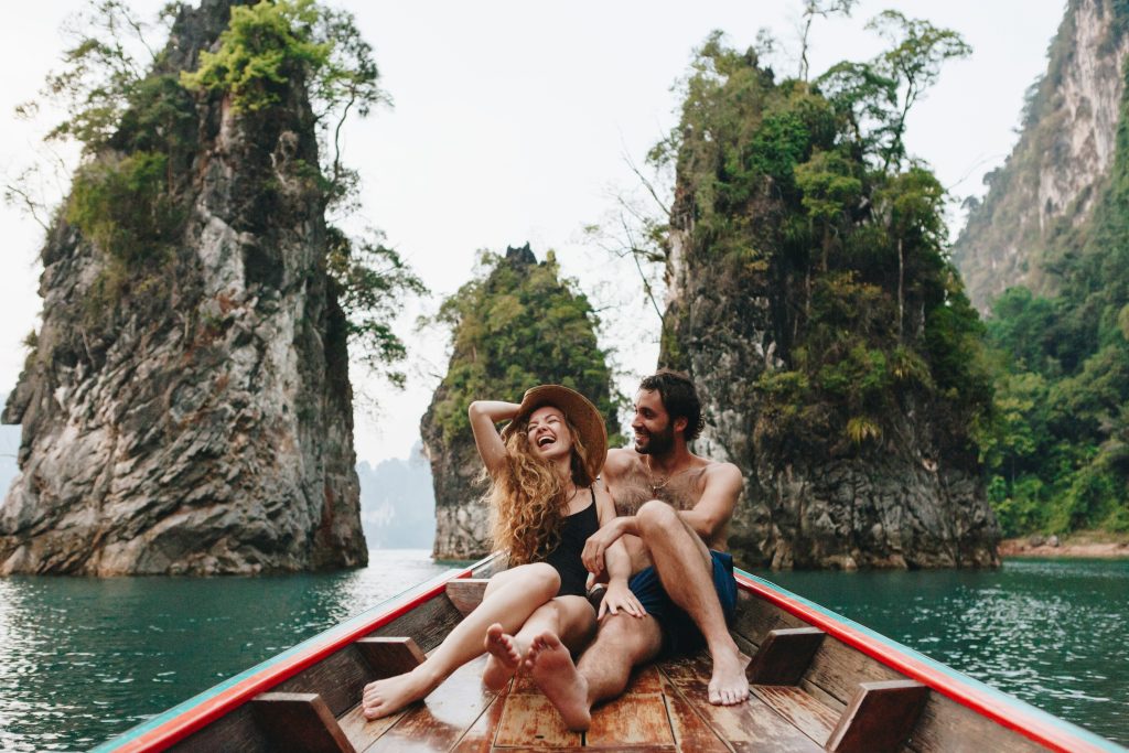 A smiling couple hugging in a canoe surrounded by rocky coastal formations, enjoying a romantic honeymoon moment