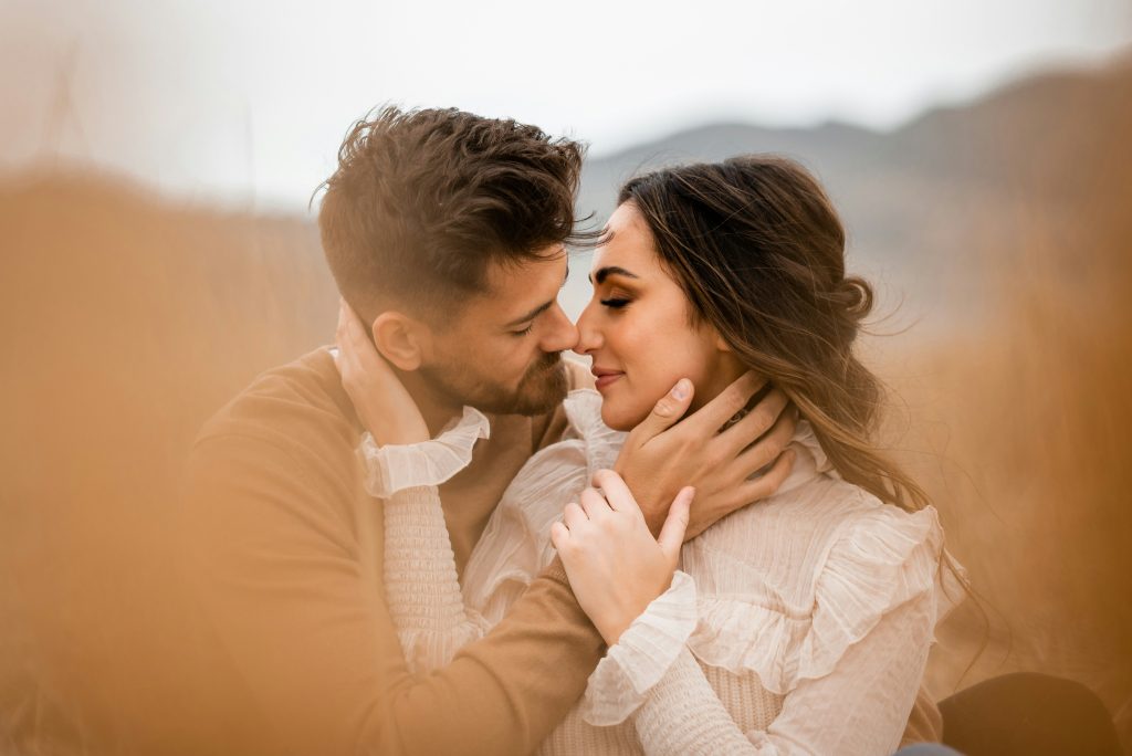 A couple standing very close outdoors on a sunny day, looking into each other’s eyes as if about to kiss
