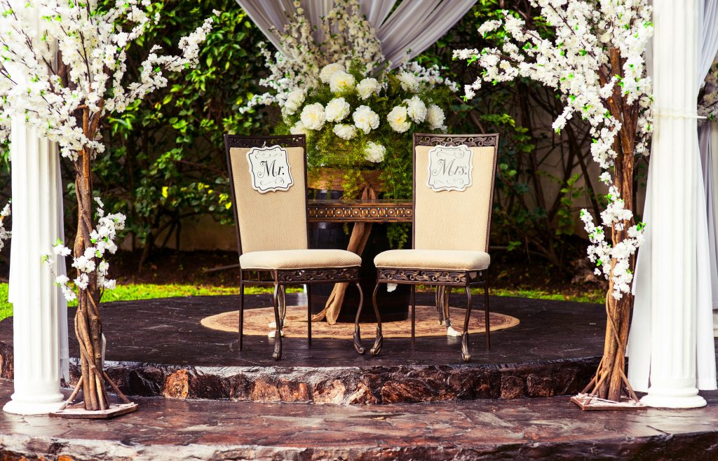 Two empty wedding chairs for the bride and groom, beautifully decorated with flowers and arranged for the ceremony