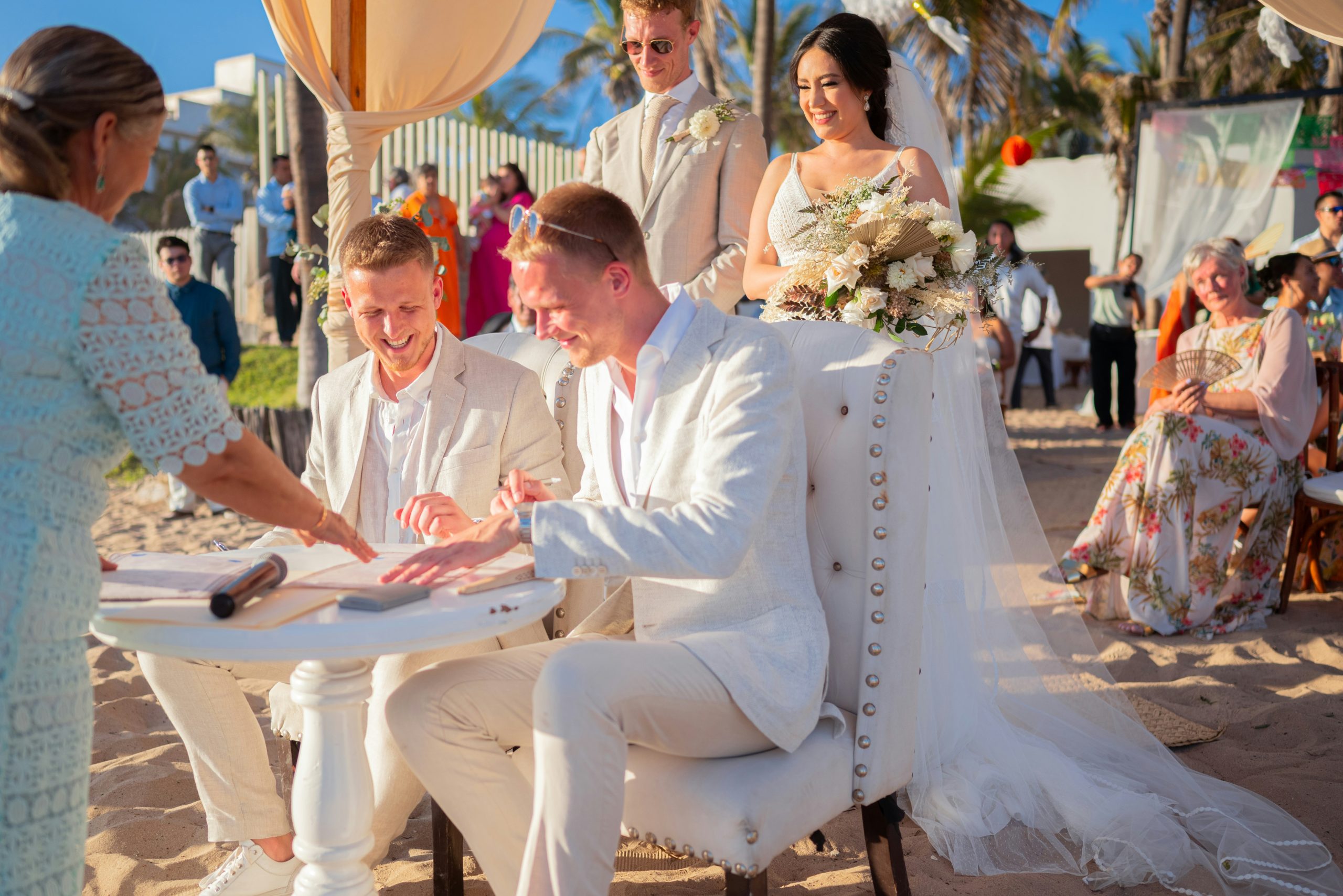 A happy gay couple signing documents during their beach wedding ceremony, smiling as they celebrate their marriage by the ocean