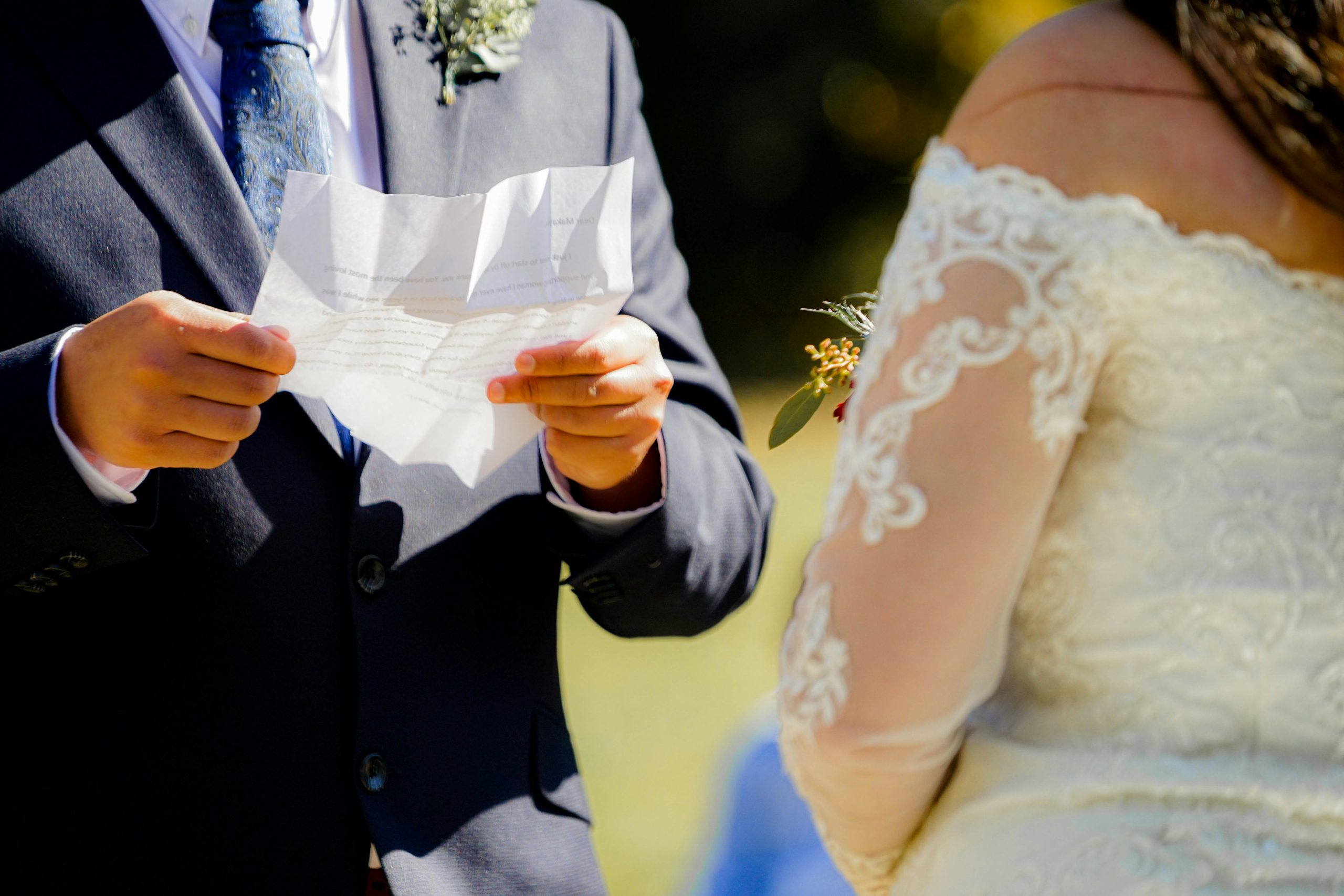 A close-up of the groom’s hands holding a folded piece of paper as he reads his wedding vows during the ceremony