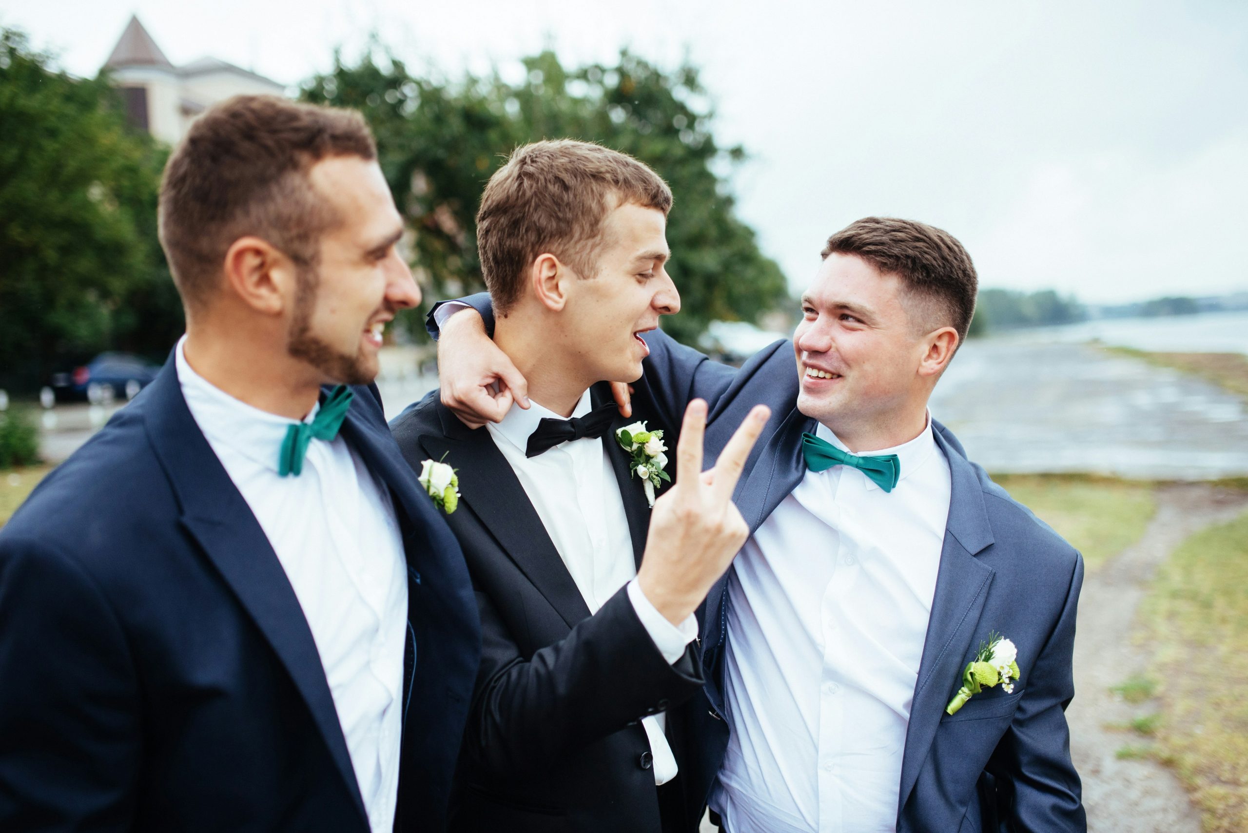 A groom standing with his two groomsmen, dressed in formal attire and sharing a moment together on the wedding day