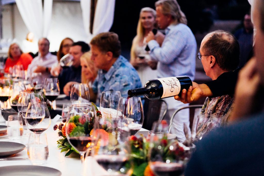 A table with several guests seated as wine is being poured, capturing a lively and social dinner setting before a wedding
