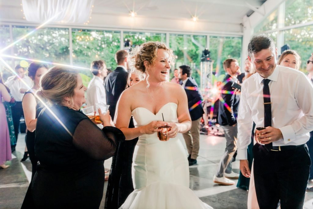 A bride and groom laughing together as an older woman dressed in black congratulates them during their wedding celebration