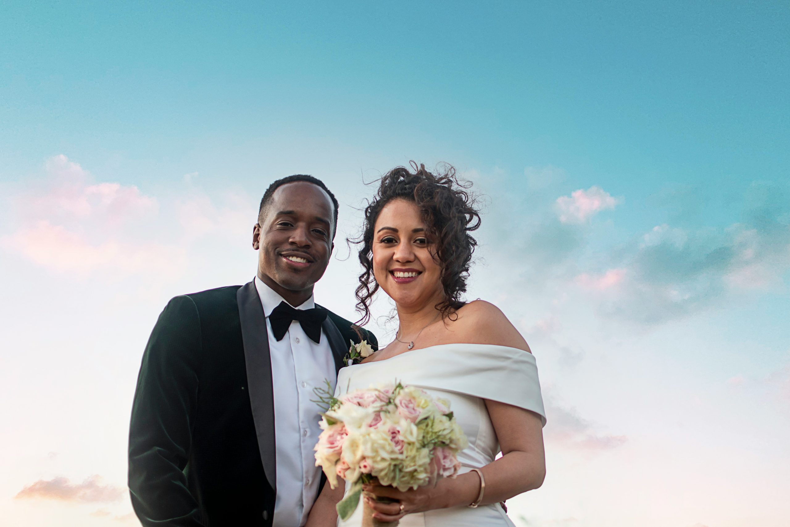 Newlyweds smiling at the camera under a blue sky A bride and groom looking at the camera on their wedding day, with a bright blue sky in the background