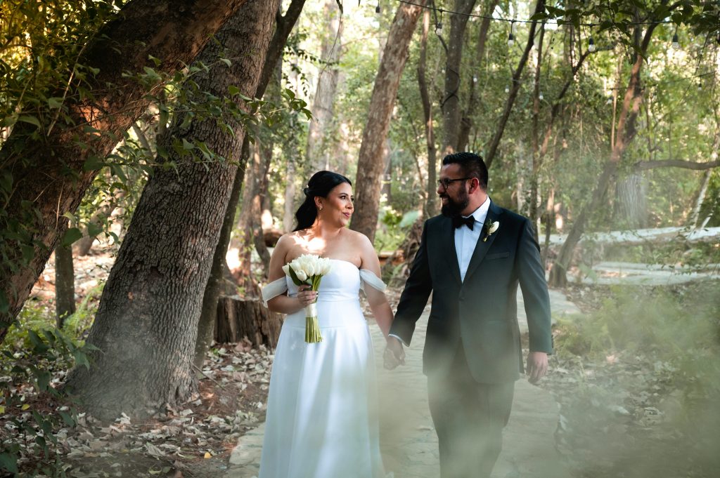 A bride and groom walking together outdoors on their wedding day in a warm, desert-like landscape, sharing a peaceful moment