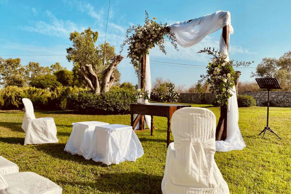 A sunny outdoor wedding venue with wide green lawns and a natural wooden altar decorated with flowers, set for the ceremony