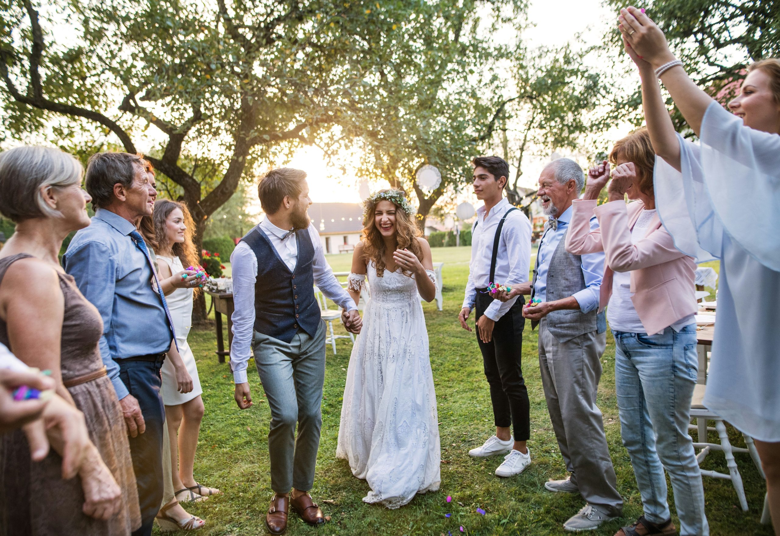 A sunny outdoor wedding where the couple stands at the center as family and friends line up to create a path for them to walk through in celebration