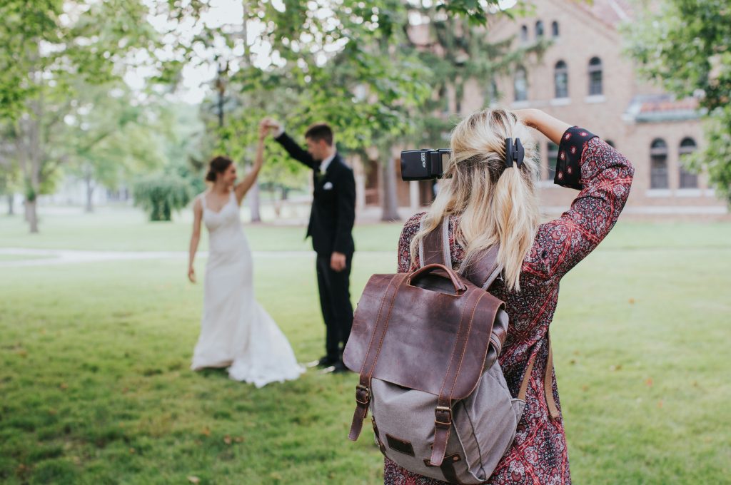 A wedding photographer guiding a couple in their wedding dress and suit while taking photos at an outdoor venue