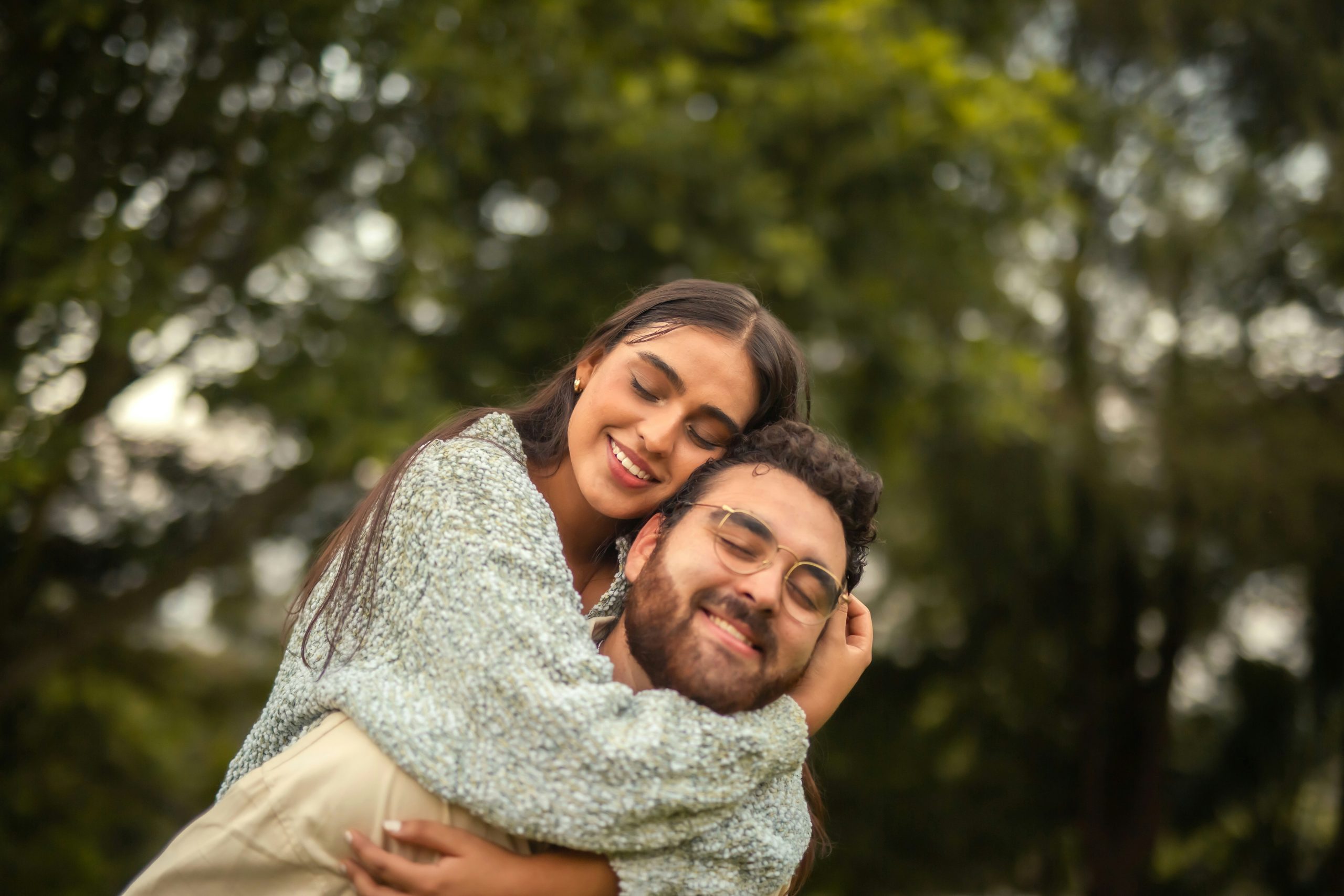 A couple sharing a piggyback moment with their eyes closed, smiling and enjoying a relaxed day together outdoors