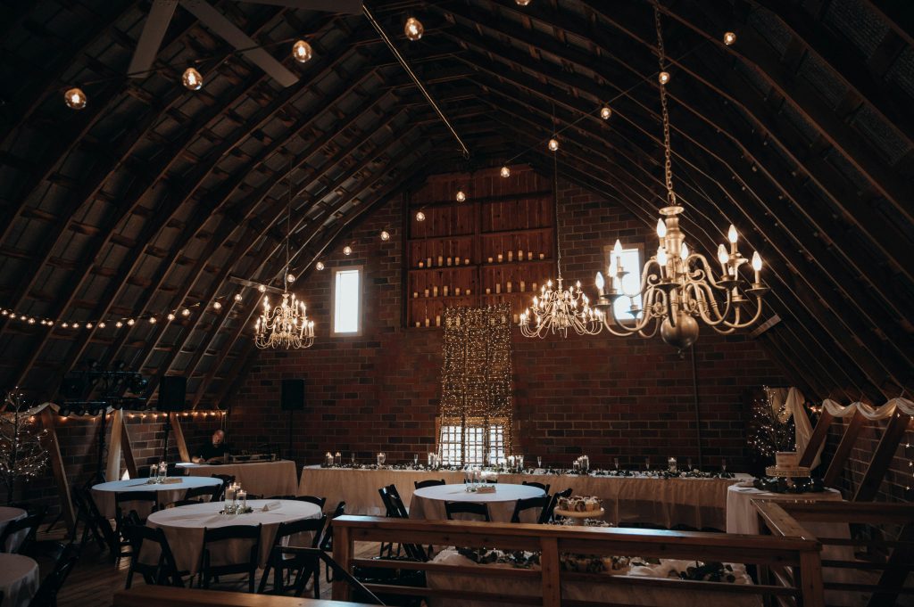A large wooden barn decorated with string lights and floral arrangements, set up as a warm and elegant wedding venue