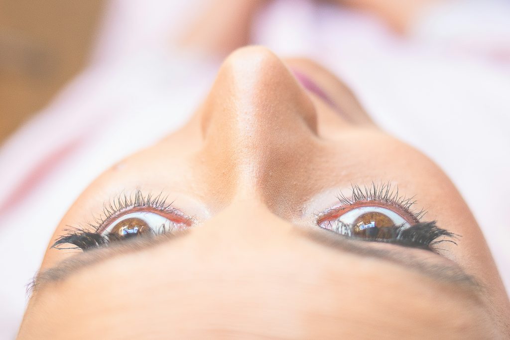 A top-down view of a bride’s face as a makeup artist applies mascara to her eyelashes during wedding preparations
