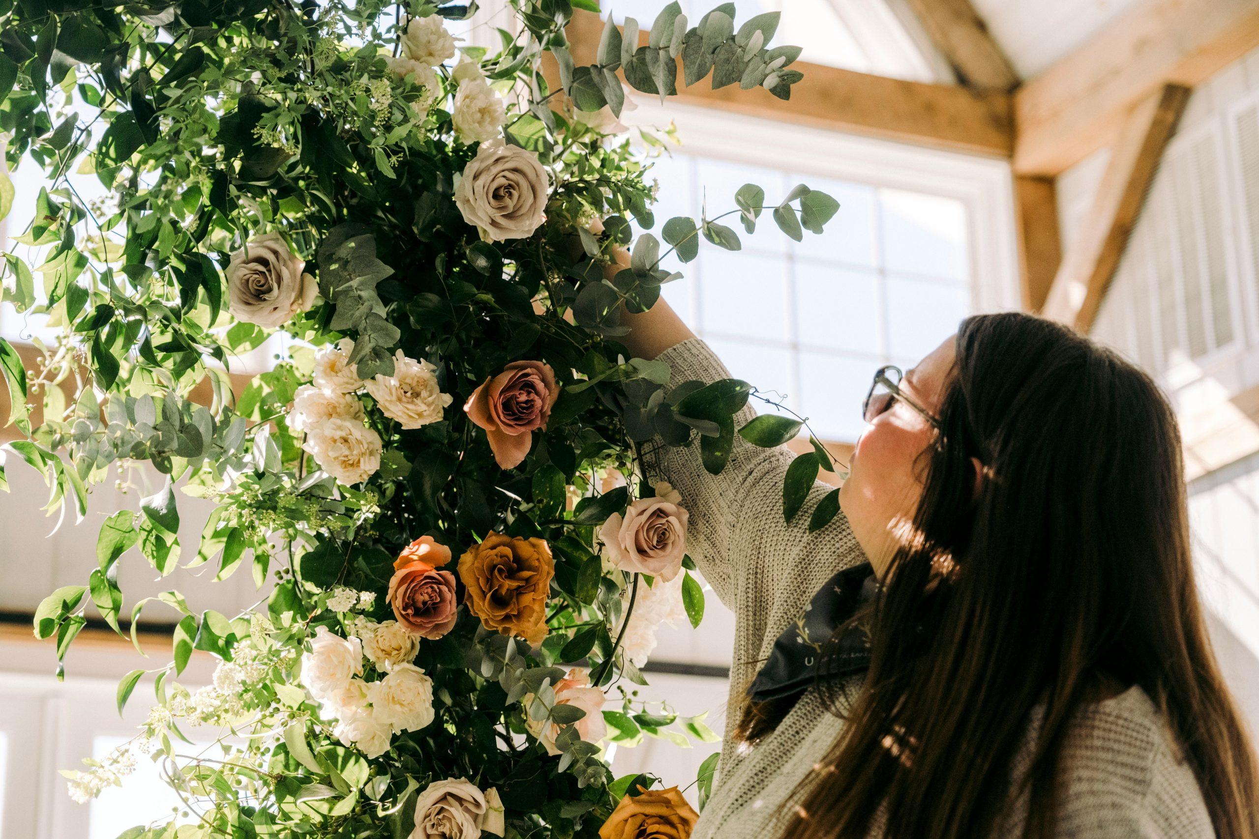 A wedding planner adjusting and arranging flowers at a venue, preparing the floral setup for the ceremony or reception