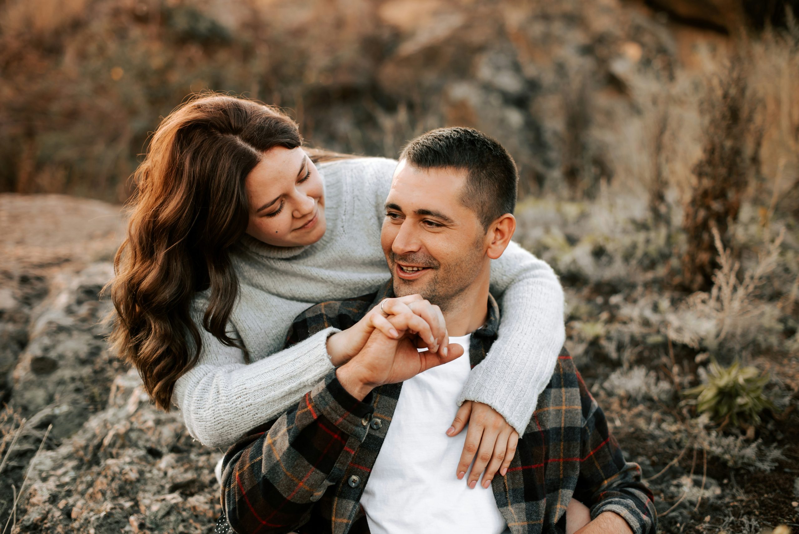 A happy couple laughing together outside with rocky scenery in the background, enjoying a joyful and carefree moment
