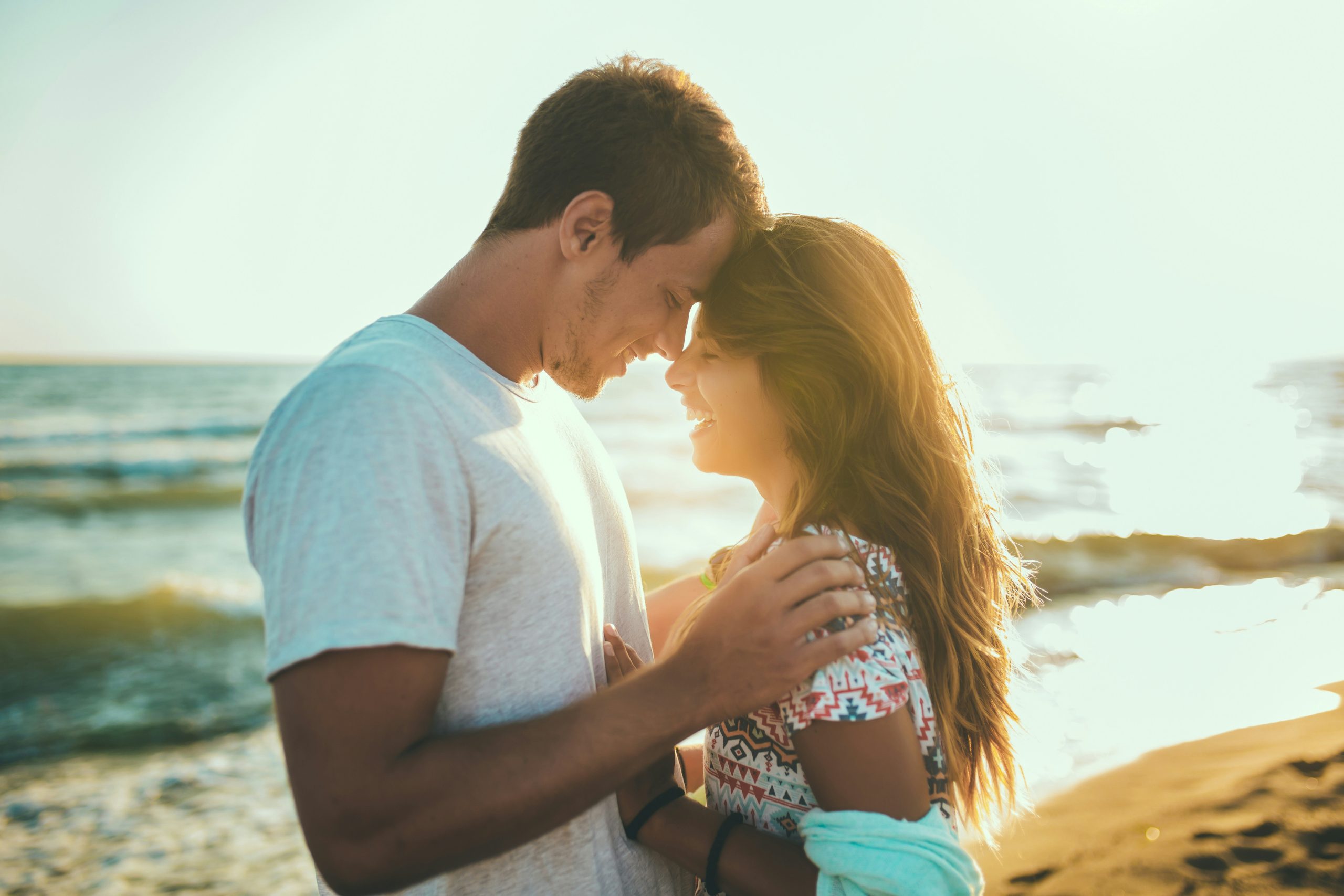 Photo of a couple with foreheads together on the beach at sunset