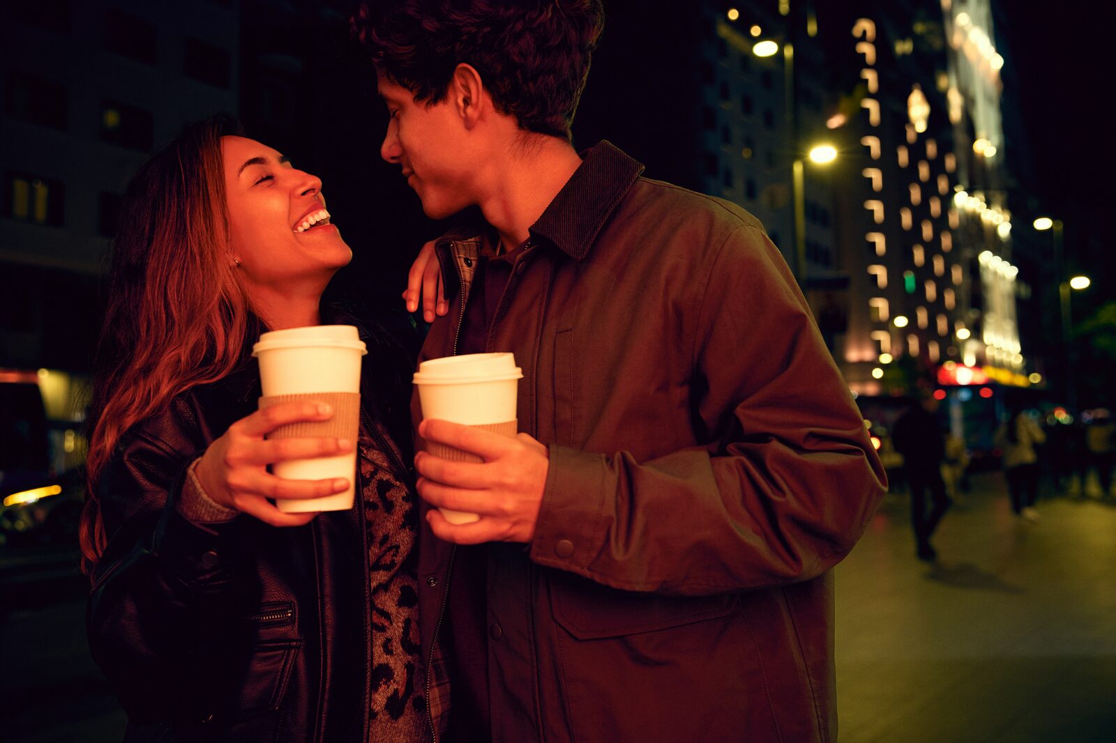 New York couple laughing with coffee cups in Times Square at night, exploring their prenup options