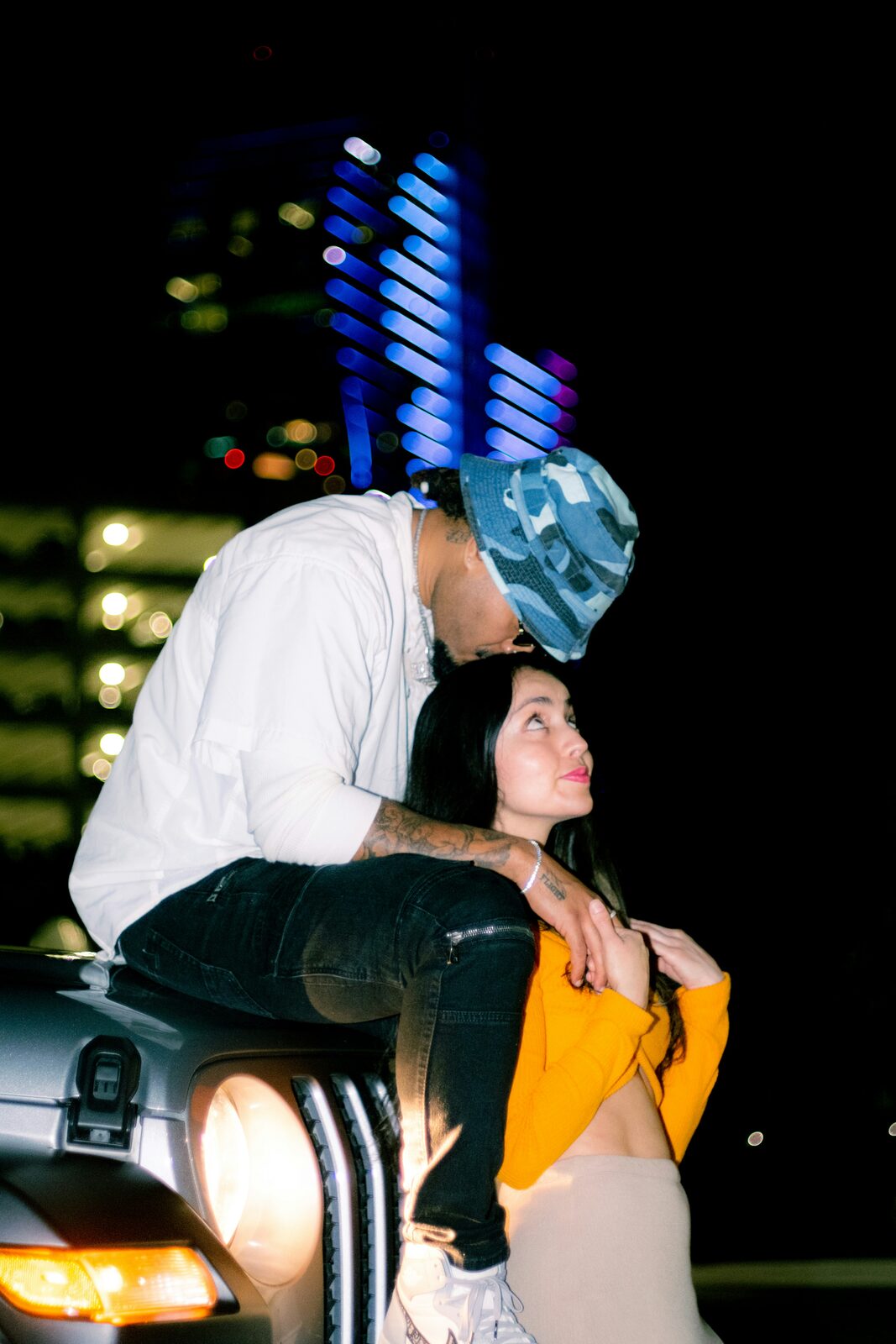 Florida couple sitting on a car hood under city neon lights, talking through marital property and alimony in their prenuptial agreement