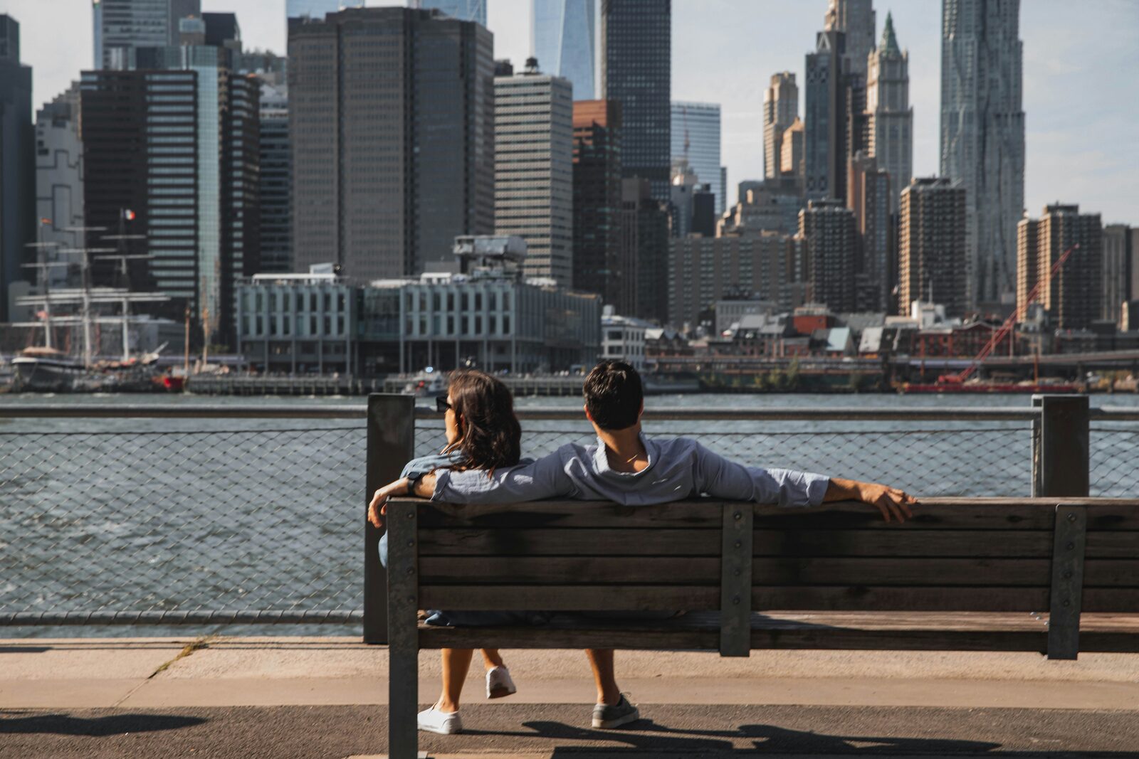 New York couple sitting on a bench at Brooklyn Bridge Park overlooking the Manhattan skyline, preparing to build their prenup