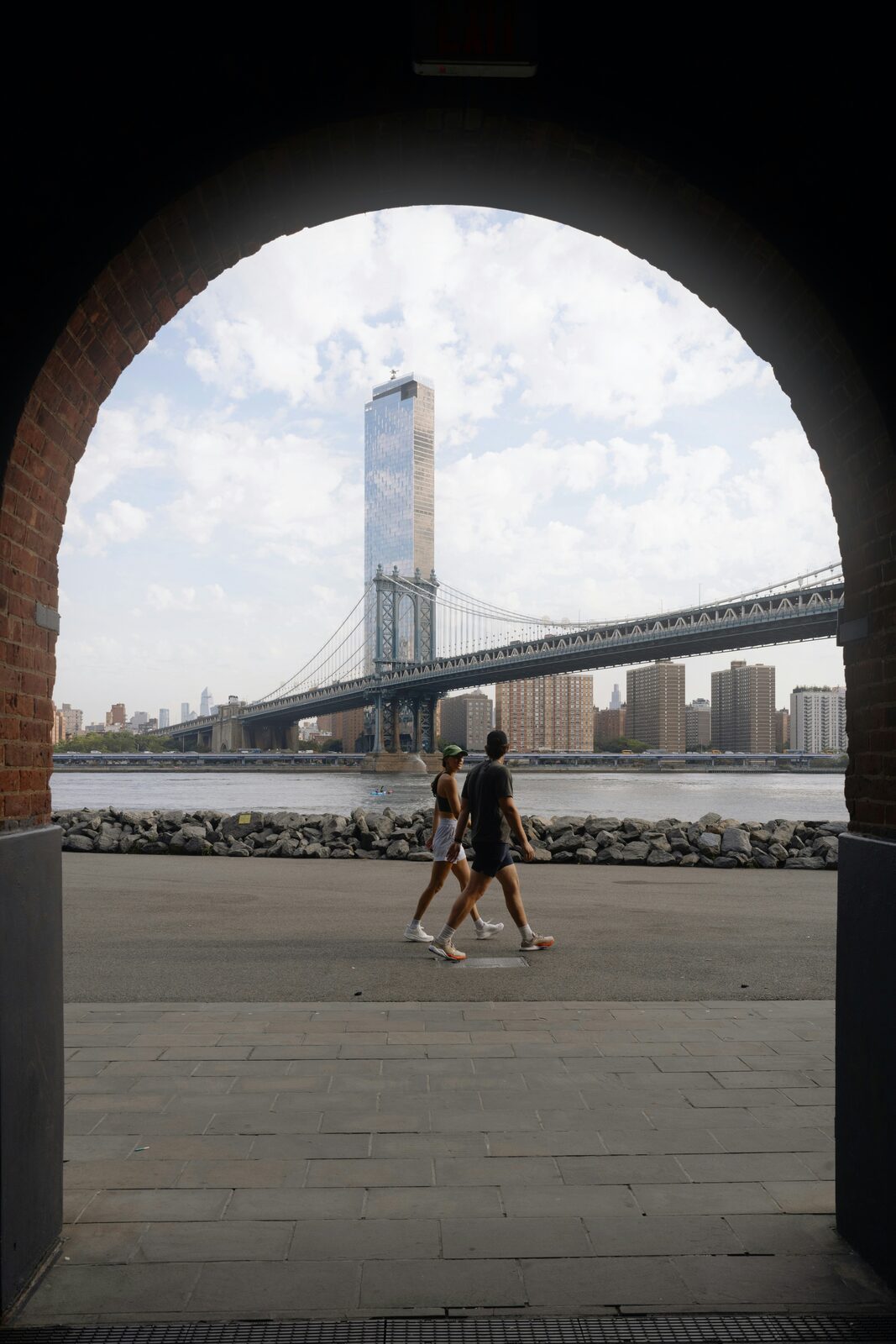New York couple walking under the Manhattan Bridge archway in Dumbo, Brooklyn, ready to protect their future with a HelloPrenup prenuptial agreement