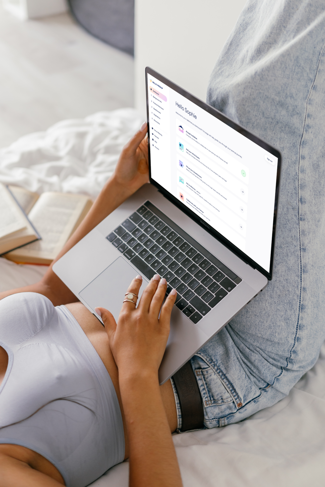 Woman on a MacBook Air starting her HelloPrenup online prenup from bed, with the couple's dashboard on screen