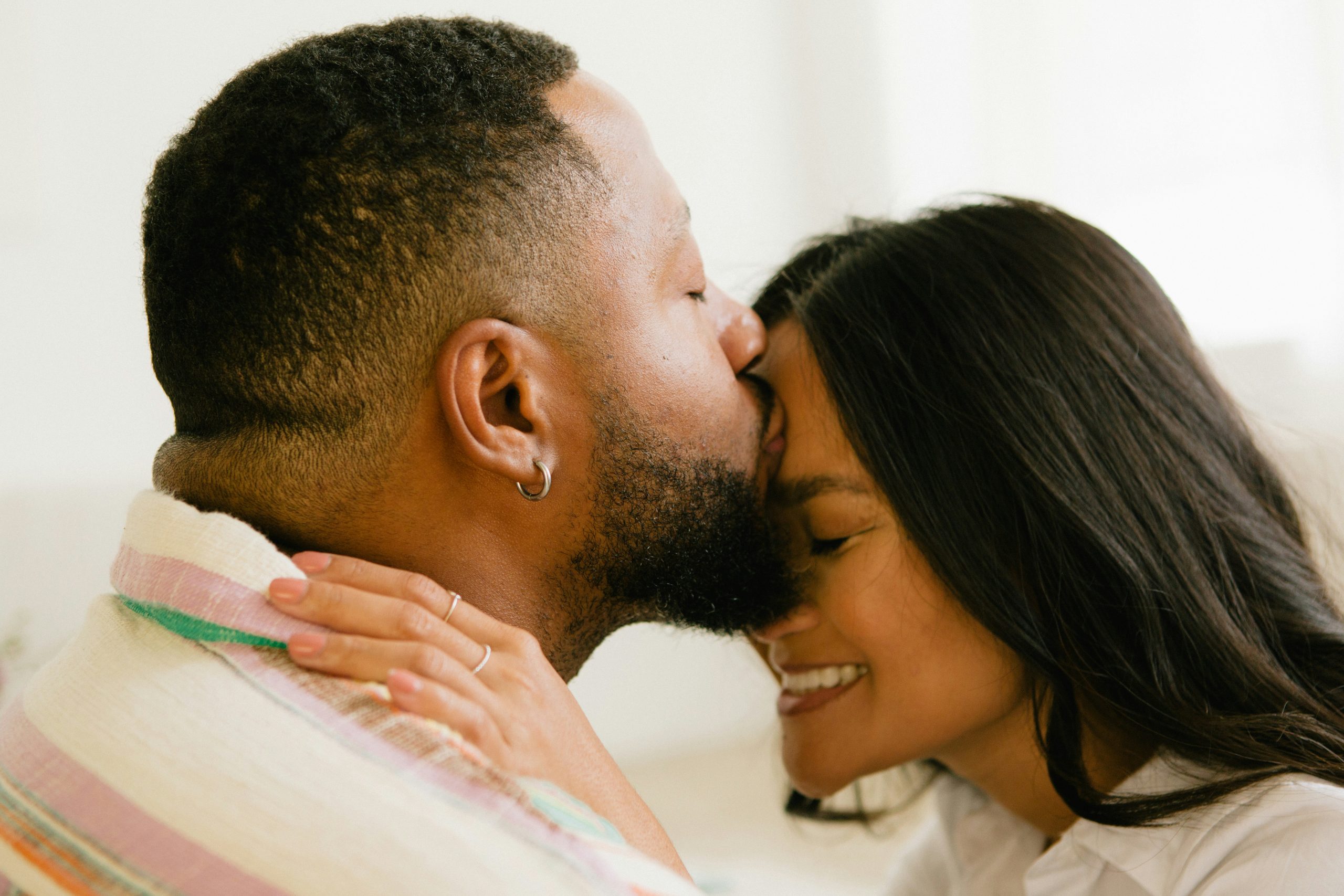 Photo of an engaged couple sharing a forehead kiss, engagement ring visible