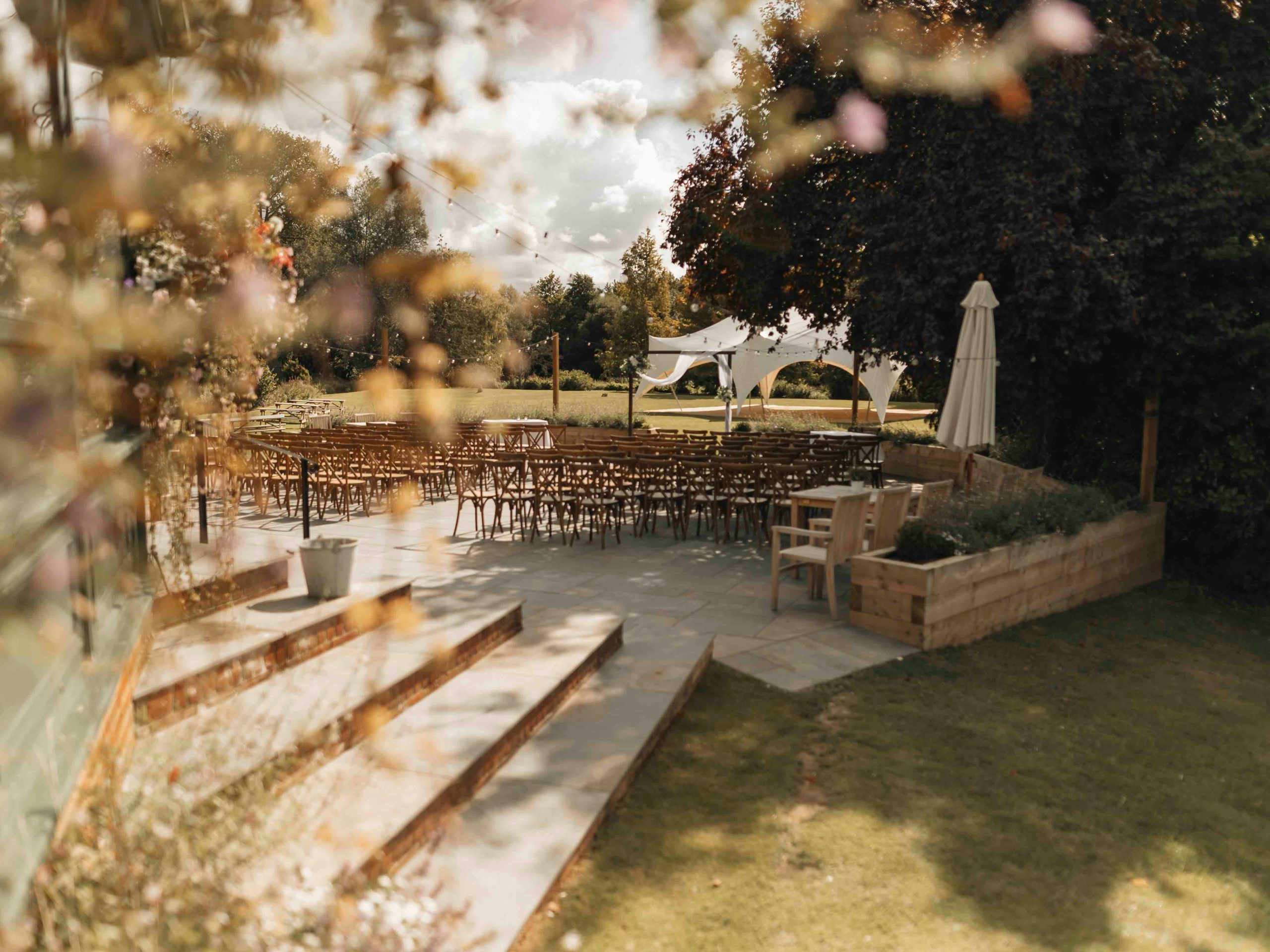 A beautifully decorated outdoor wedding venue with elegant floral arrangements, seating, and bright sunshine creating a romantic atmosphere