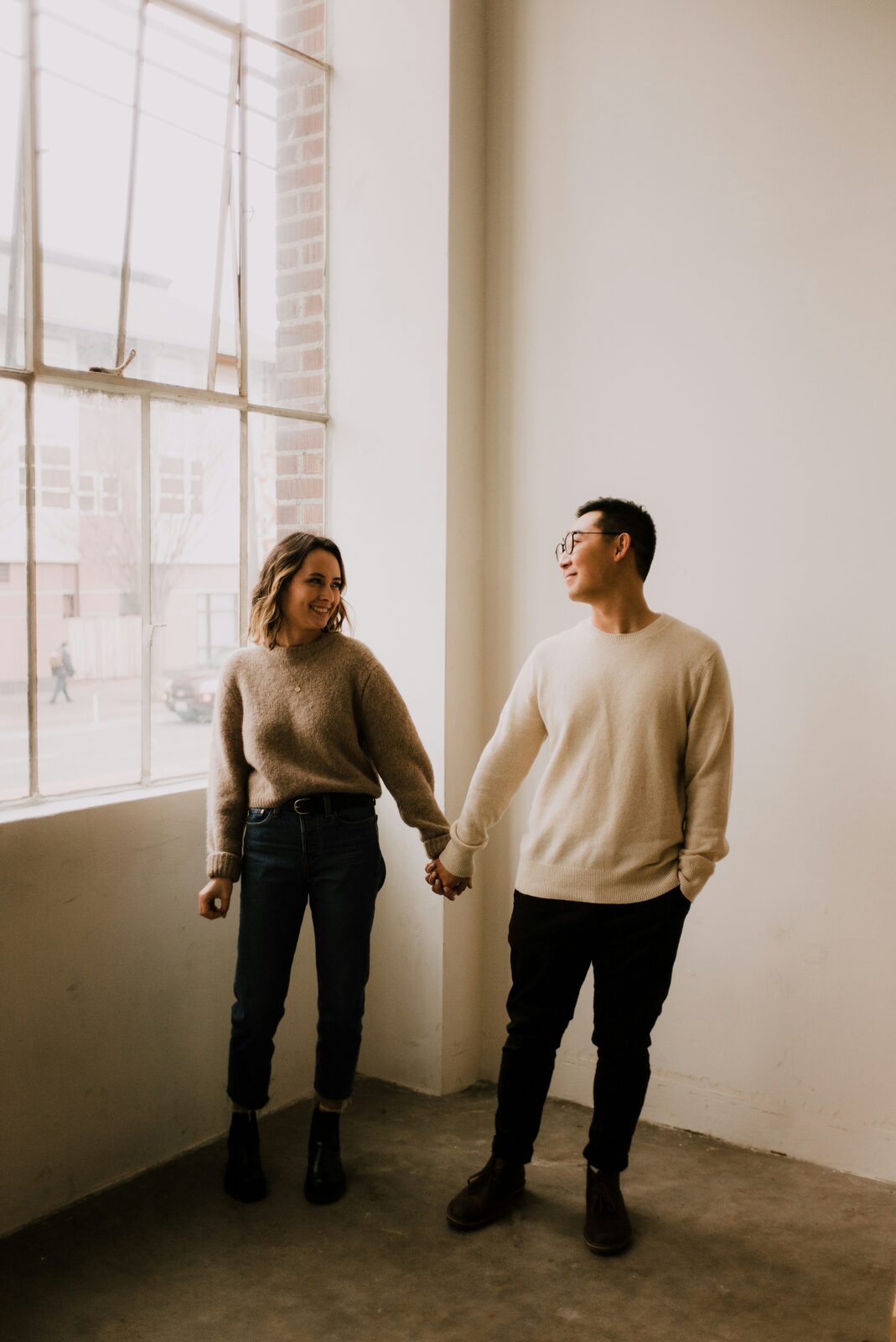 Washington couple holding hands by a warehouse loft window, planning their prenup