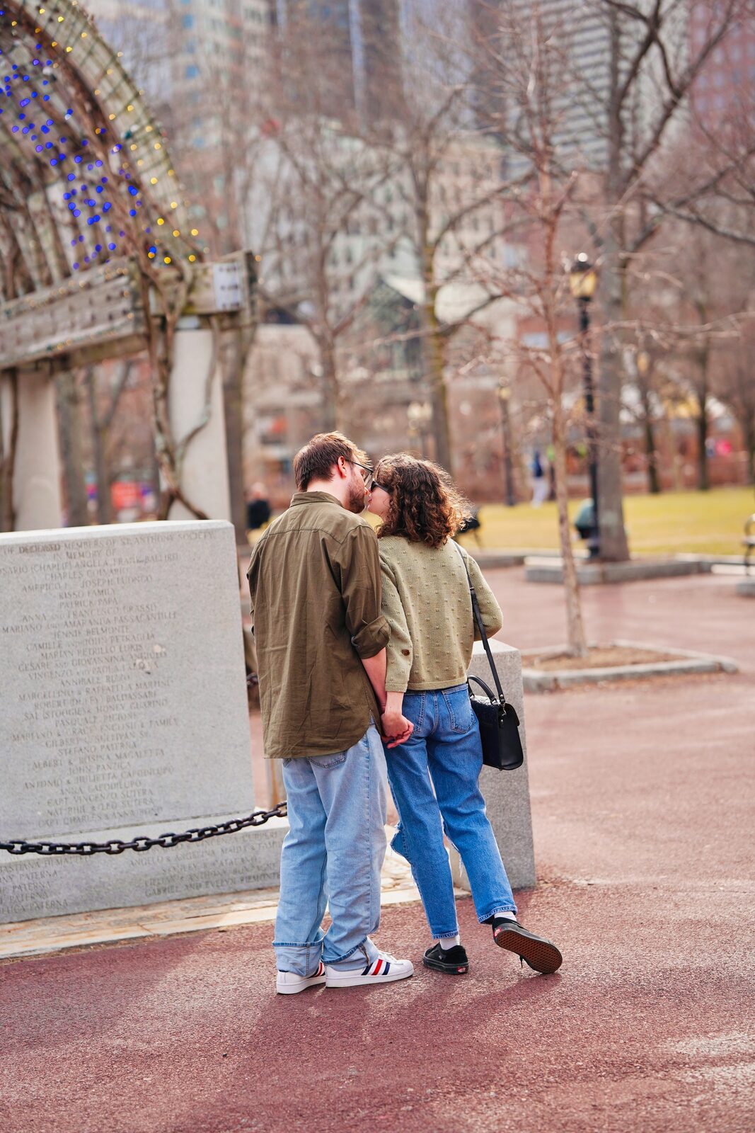 Massachusetts couple kissing in Boston Common with the city skyline behind them, celebrating their engagement