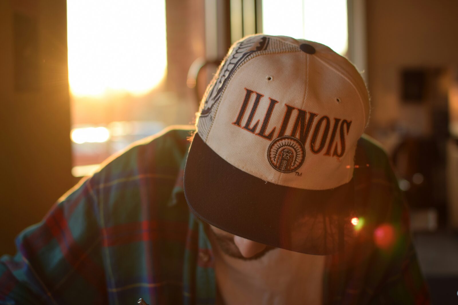 Man wearing a vintage Illinois cap and flannel shirt in golden-hour window light after building his prenup with HelloPrenup