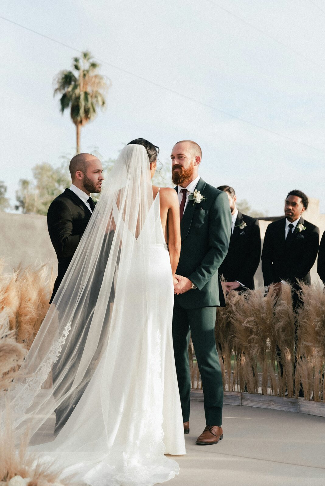 Couple exchanging vows at an outdoor desert ceremony framed by pampas grass