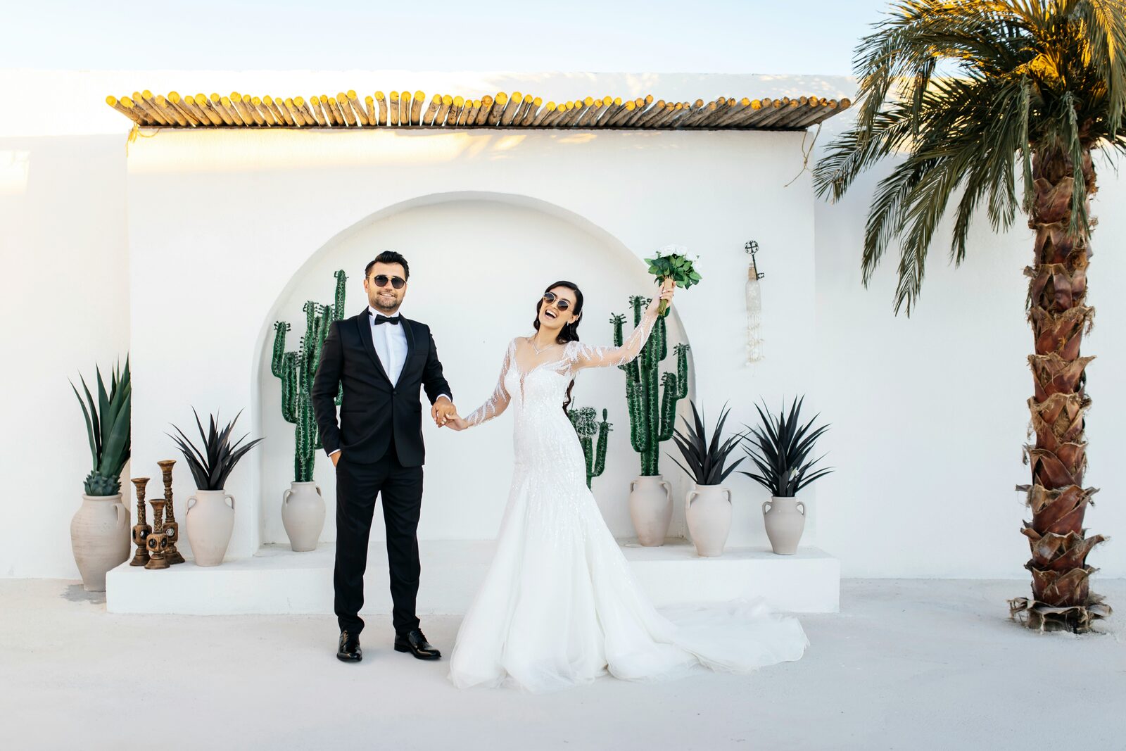 Playful bride and groom in sunglasses by a desert cactus arch, exploring their prenup options